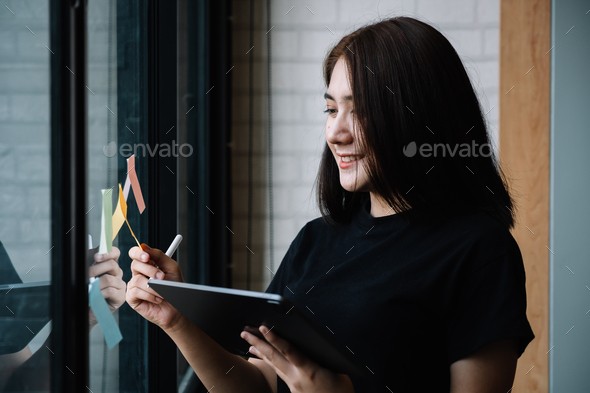 business woman using tablet during post it notes idea discussing and planning in glass wall at