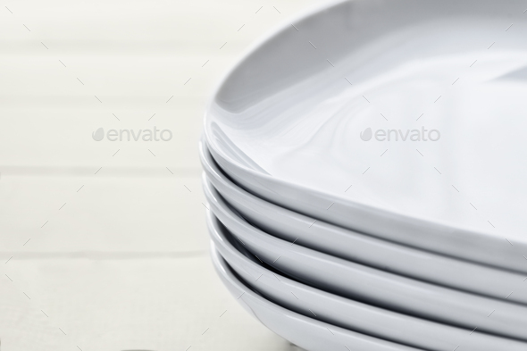 Stack pile of rectangular white ceramic dishes with rounded edges on wooden white background.