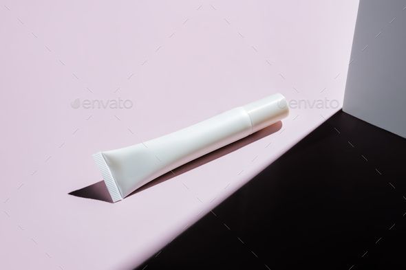 White unbranded plastic tube with eye cream or face serum on pink background with hard shadows.