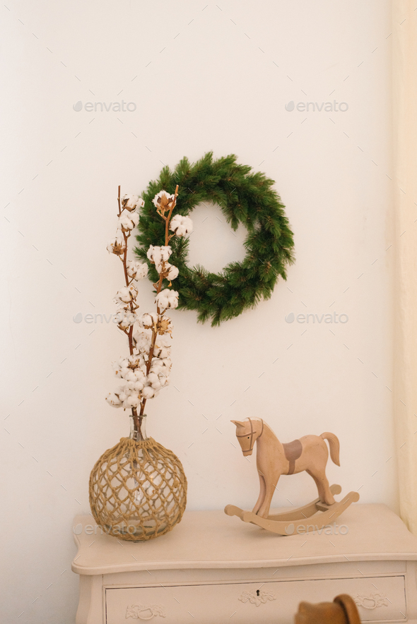 Cotton branches in a vase, a toy wooden horse on the chest of drawers, a Christmas wreath on wall