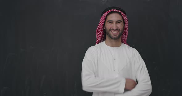 Portrait of Young Arabian Man in Traditional Clothes in Front of Black Chalkboard alt