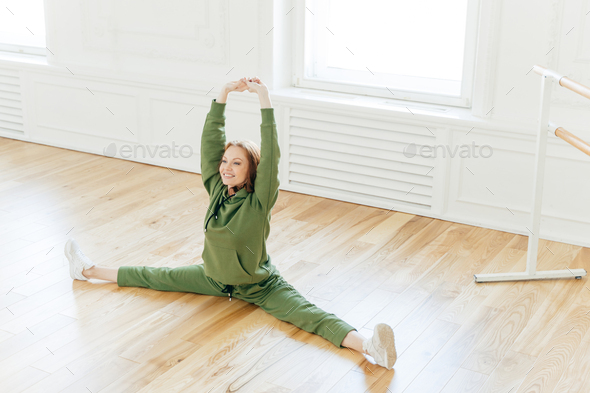 Strong Flexible Curly Red Haired Woman Does Side Leg Split Raises Hands Wants To Have Perfect