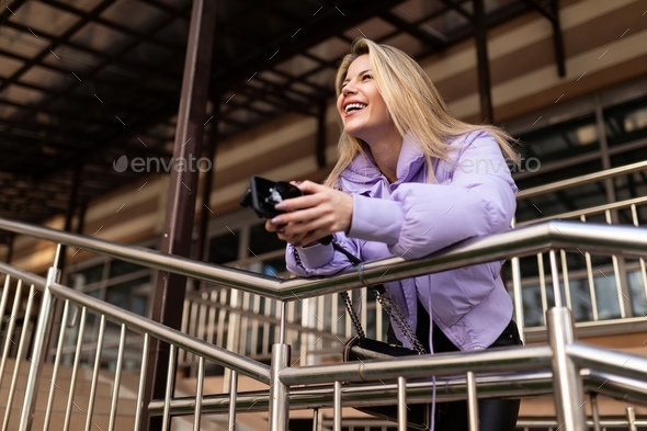 an adult woman in a lilac jacket laughs looking forward leaning on the railing of the stairs