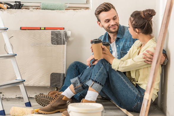 young couple holding paper cups and smiling each other while sitting on ...