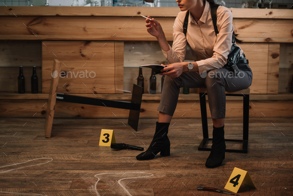 cropped view of smoking female detective sitting at crime scene with evidence markers and dead body