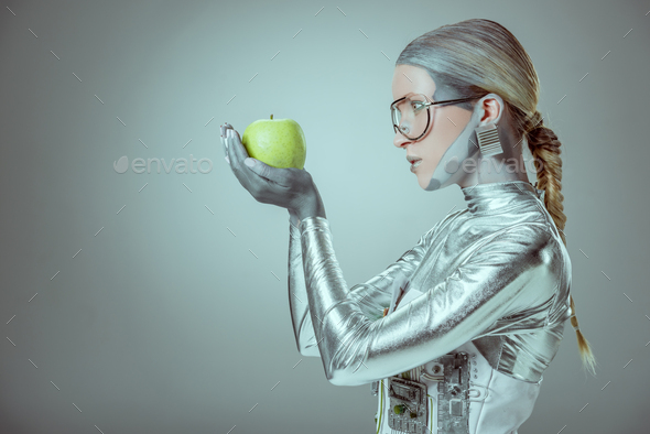 side view of woman robot holding green apple isolated on grey, future technology concept