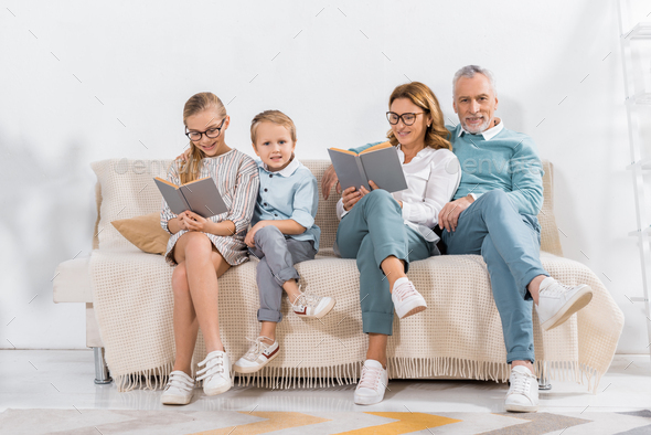grandchildren and grandparents reading books on sofa at home