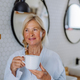 Beautiful senior woman in bathrobe drinking tea in bathroom, relax and wellness concept. - PhotoDune Item for Sale