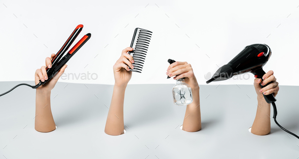 cropped shot of women holding hairstyle tools through holes on white