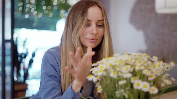 Blonde Woman Looking and Touching Beautiful Bouquet of Chamomile Flowers alt