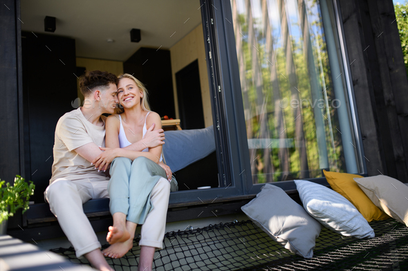 Young couple sitting and cuddling in hammock terrace in their new home ...