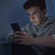 Focus caucasian teenage boy using mobile phone while sitting at night in his room - PhotoDune Item for Sale