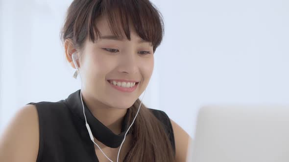 Young asian woman smiling sitting using laptop computer listening music with earphone. alt