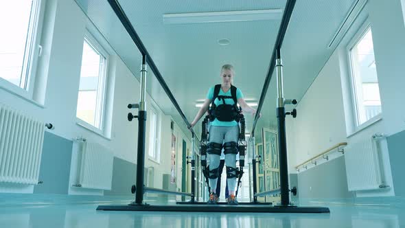 Handicapped Woman is Walking in the Exosuit with Medical Aid alt