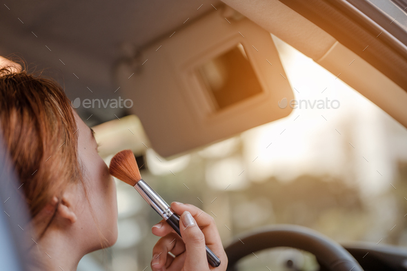 Asian women applying makeup in interior car with looking mirror using brush make up.She hurriedly
