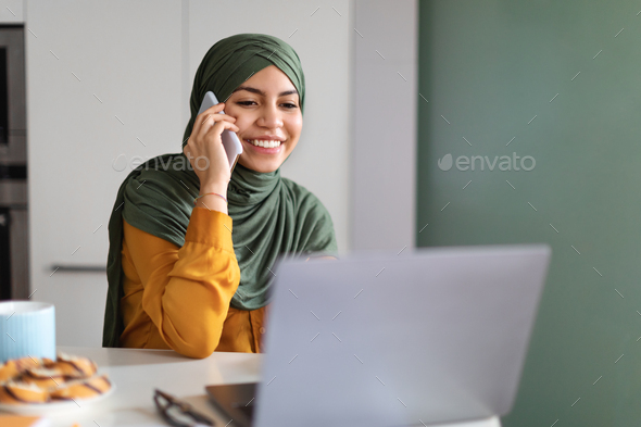 Smiling Mulsim Woman Using Laptop And Talking On Cellphone At Home - Stock Photo - Images