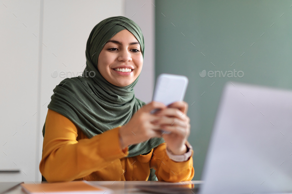 Smiling Arab Woman In Hijab Browsing App On Smartphone In Office - Stock Photo - Images