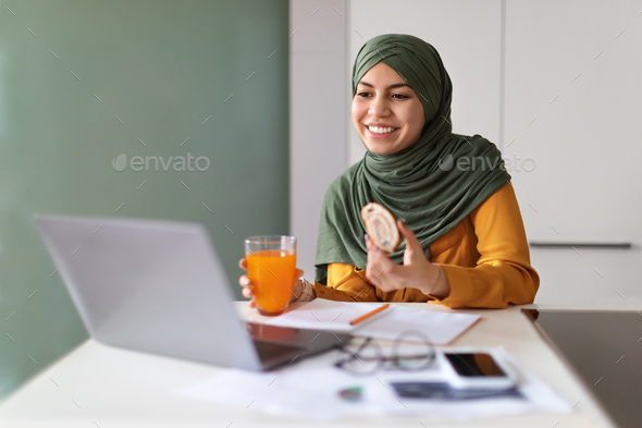 Young Muslim Woman Eating Snacks In Front Of Laptop At Home - Stock Photo - Images