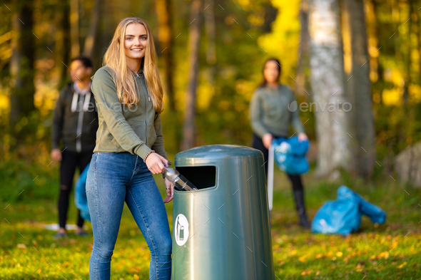 Smiling young woman putting bottle in garbage bin - Stock Photo - Images