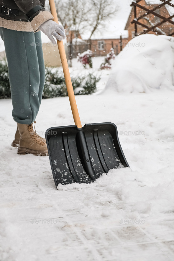 Close-up of a woman cleaning and clearing snow in front of the house on a sunny and frosty day. Clea - Stock Photo - Images