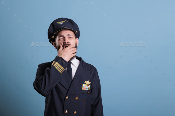 Tired airplane pilot yawning, covering open mouth with hand - Stock Photo - Images