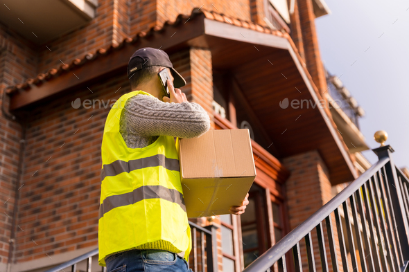 Package delivery man from an online store, with a box in hand on the stairs of the house