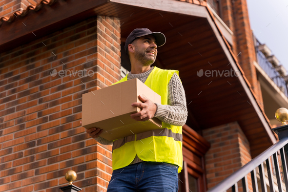 Package delivery man from an online store, with a box in hand on the stairs of the house