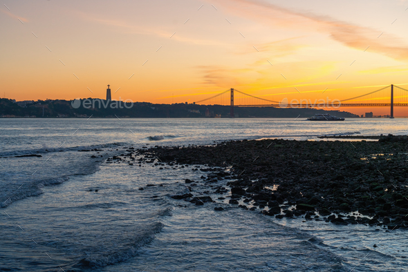 Tagus River at sunset with 25 de Abril Bridge and Sanctuary of Christ the King - Lisbon, Portugal - Stock Photo - Images