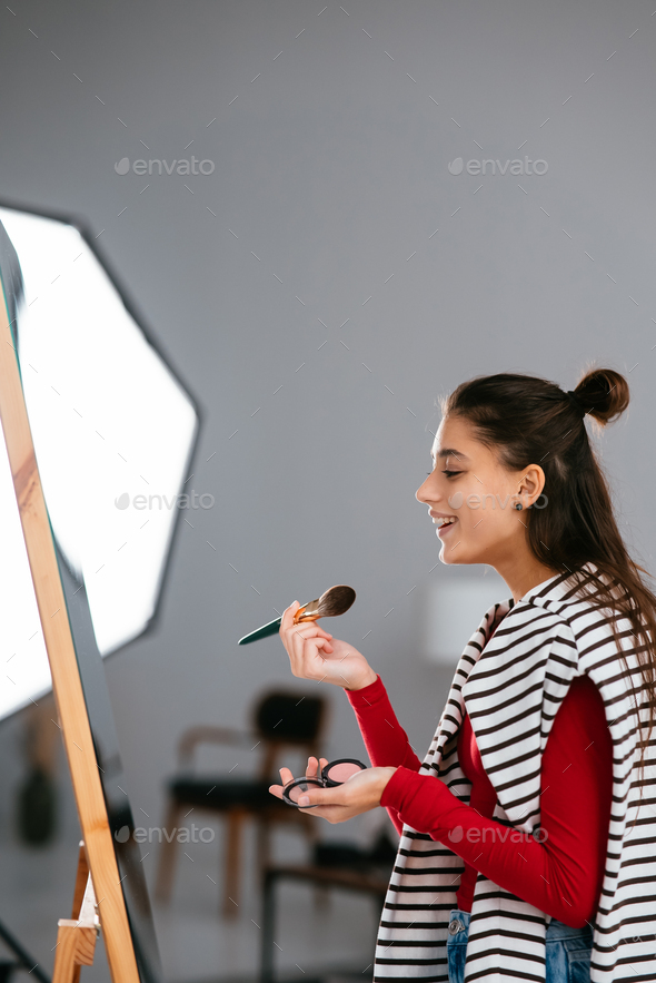 Young woman applies makeup on her face in front of the mirror - Stock Photo - Images