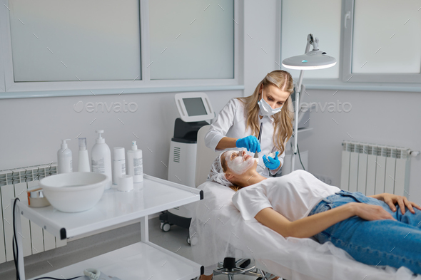Beautician applying clay face mask on woman face side view