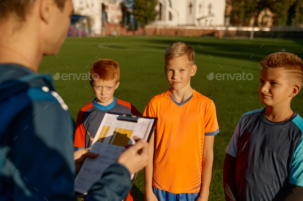 Football trainer talking to team of little players on field during break