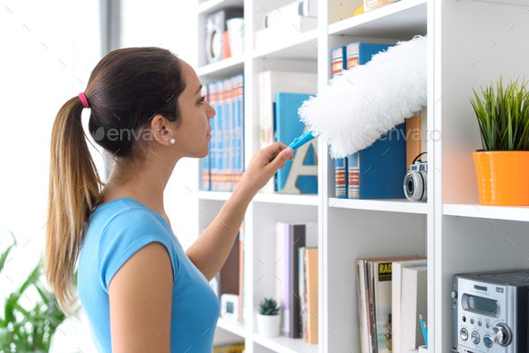 Woman dusting a bookcase at home