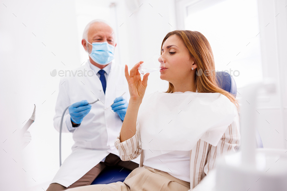 Woman washing up mouth while doctor fixing her tooth at dentist office