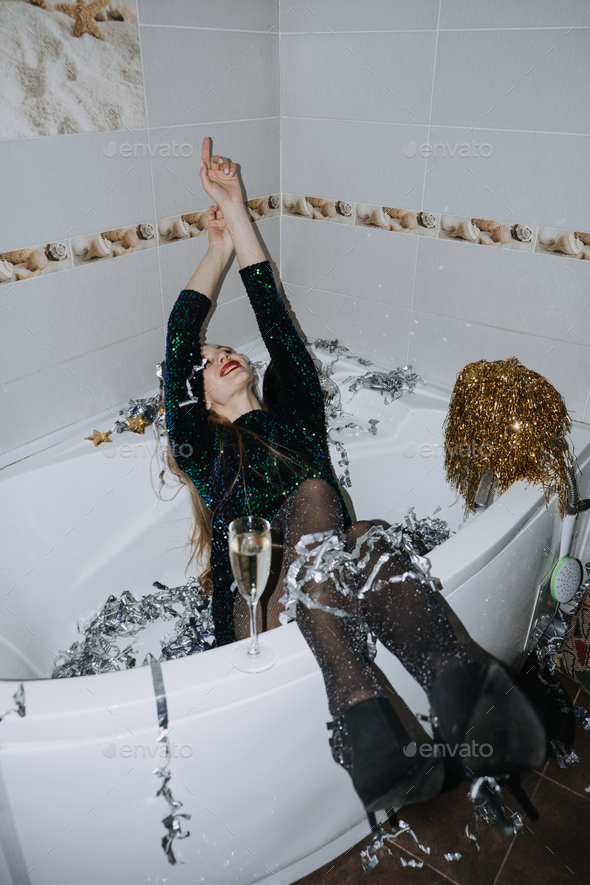 Happy young woman in evening dress sitting in the bathtub drinking champagne and having fun. - Stock Photo - Images