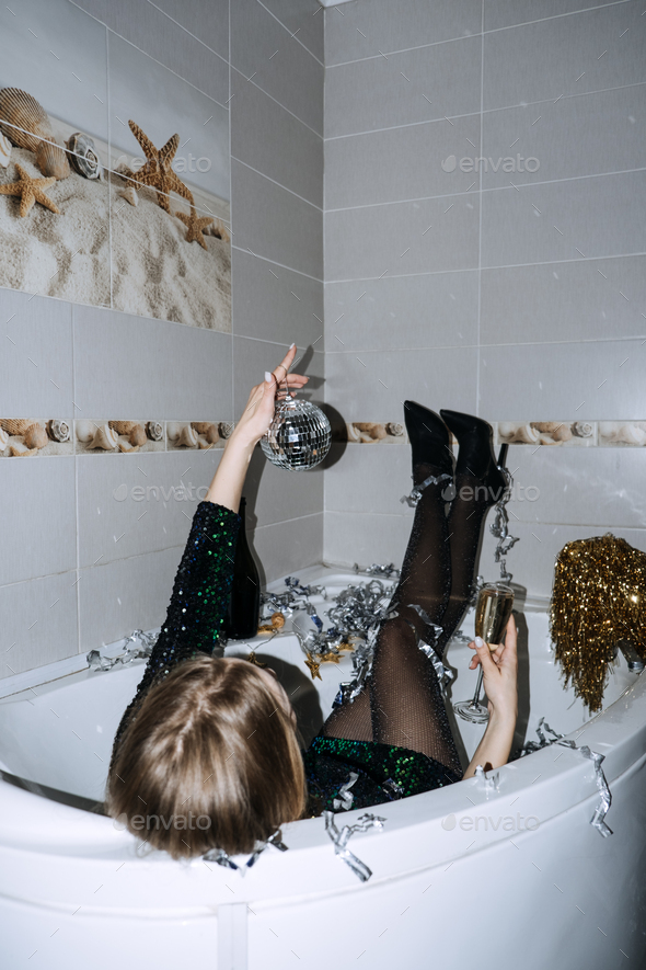 Happy young woman in evening dress sitting in the bathtub drinking champagne and having fun - Stock Photo - Images