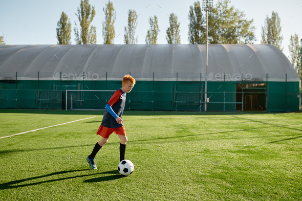 Elementary age football player kicking ball training along on soccer field - Stock Photo - Images