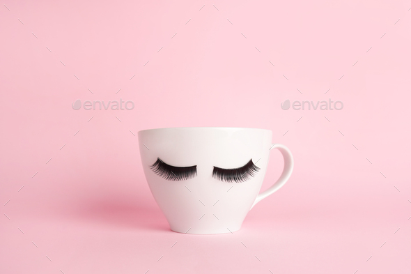 White cup coffee or tea mug with false lashes on a pink backgroun