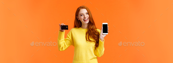 Shopping, online and finance concept. Cheerful young redhead female opened bank account, holding