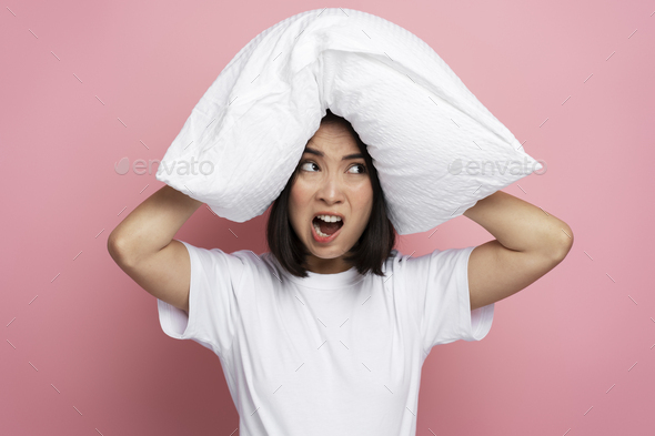 Nervous asian woman putting pillow at her head and feeling angry of ...