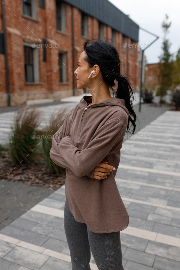Cute brunette female in brown hoodie and leggings standing on the city street