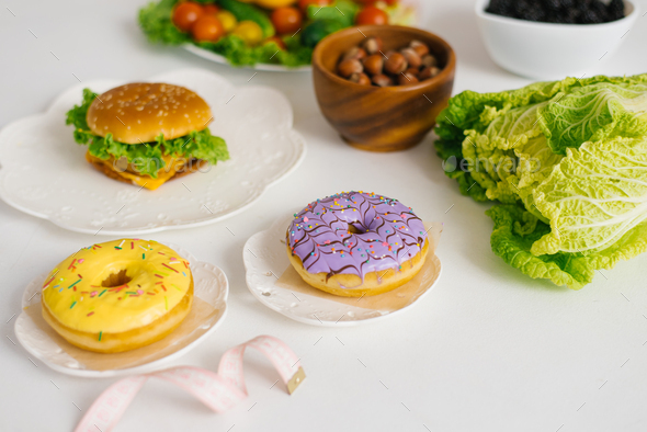 Conceptual photo of healthy and unhealthy food with measuring tape. Fruits and vegetables vs donuts