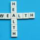 Wealth health word made from crossword square letter tiles on blue background. - PhotoDune Item for Sale