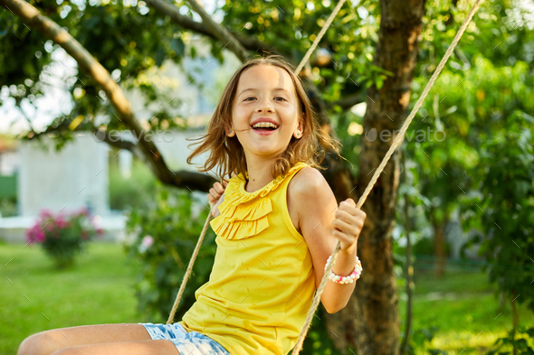 Happy barefoot laughing child girl swinging on a swing in sunset summer day - Stock Photo - Images