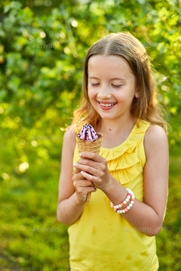 Happy girl with braces eating italian ice cream cone smiling while resting in park on summer day - Stock Photo - Images