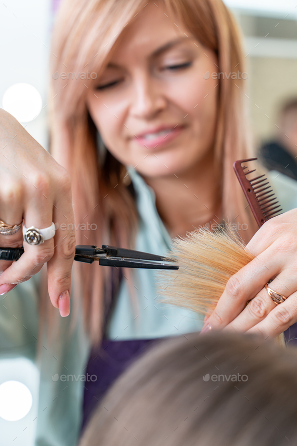 Hairdressers hands holding scissors and comb and cutting blond hair of
