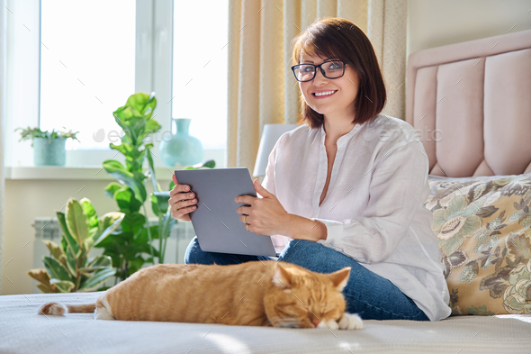 Middle aged woman at home on couch with laptop and cat - Stock Photo - Images
