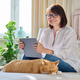 Middle aged woman at home on couch with laptop and cat - PhotoDune Item for Sale
