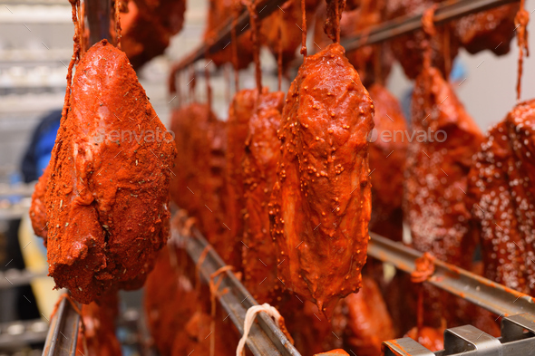 pieces of pork delicacies in paprika and spices are hung on a metal rack in a meat-packing plant or