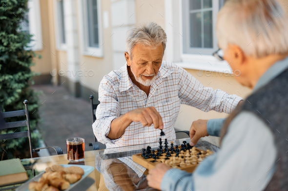 Elderly man playing chess with his friend in backyard of a nursing home.