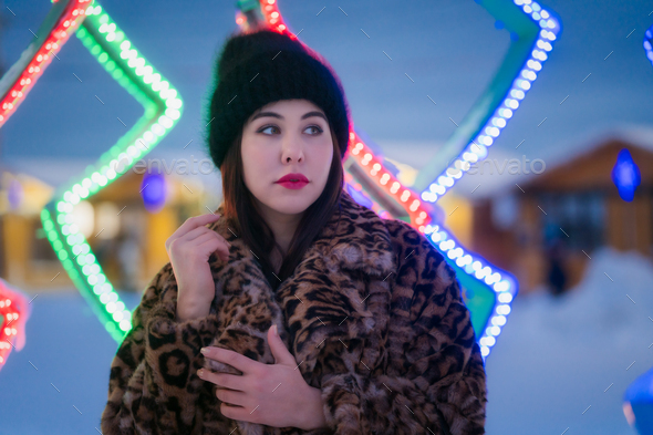 Authentic woman in fur coat with leopard pattern standing on background Christmas lights decorations - Stock Photo - Images